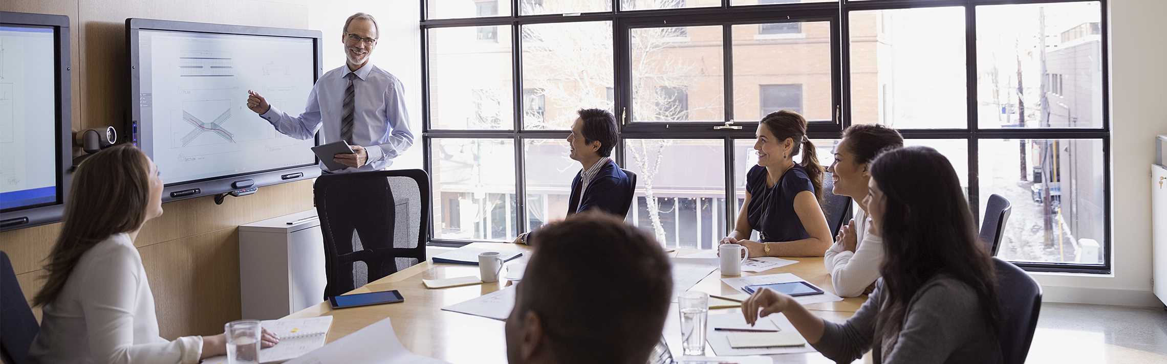 Businessman leading a meeting at a monitor in conference room.